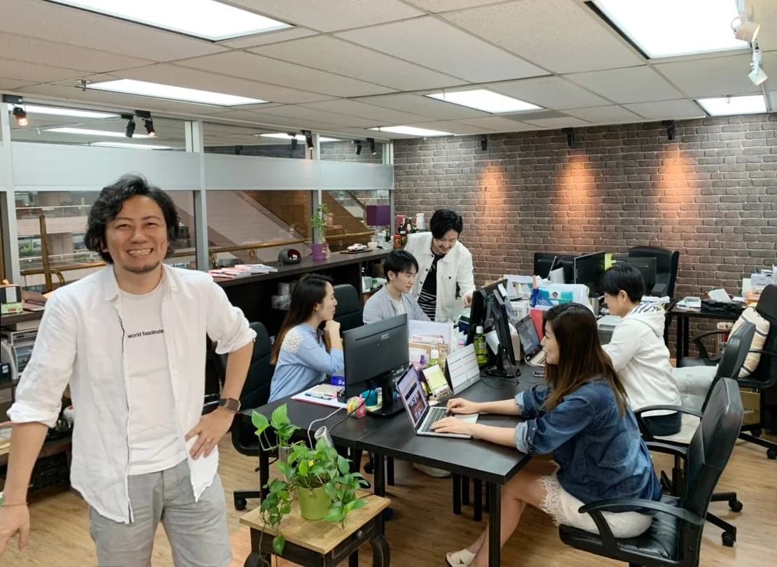 レンガ壁の台北のオフィスで、机に向かうスタッフと、手前で笑う代表