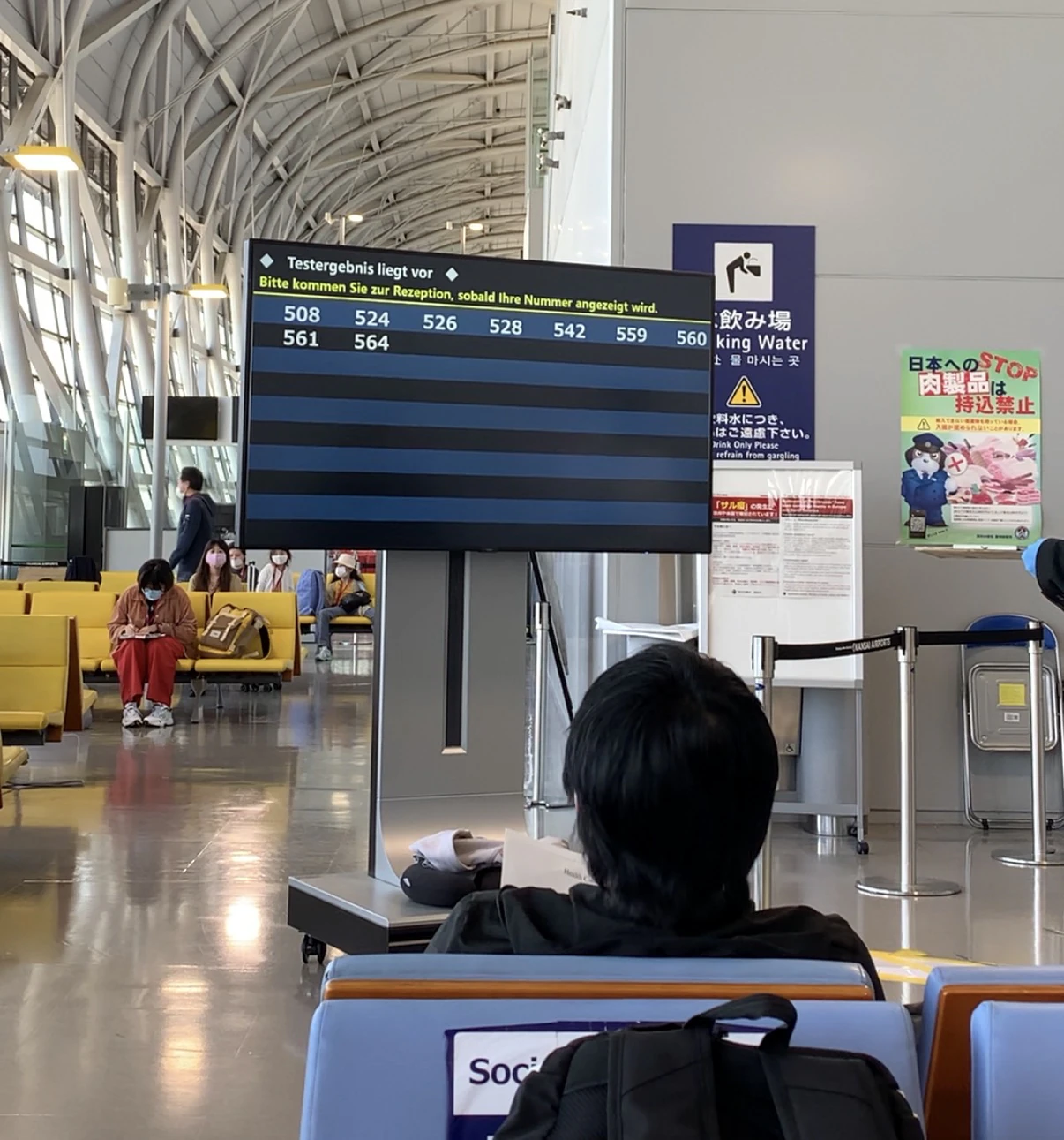 機場的等候區,坐在顯示檢驗結果的電子看板前的人
