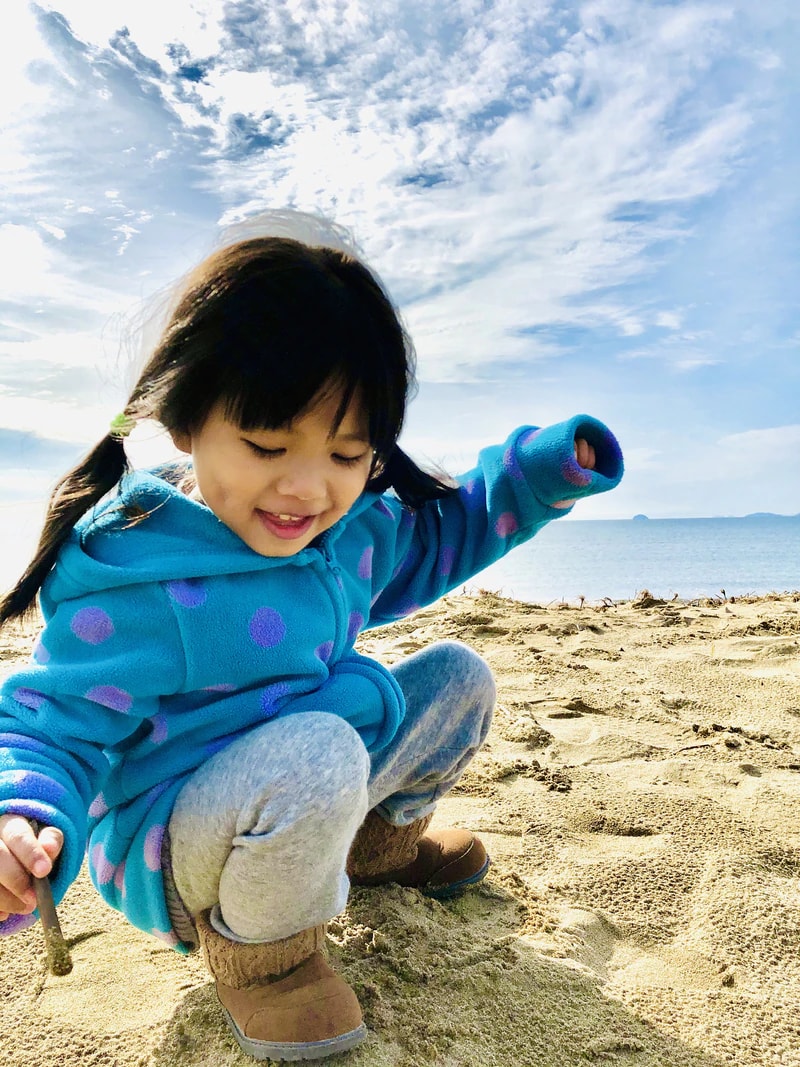 在海邊的沙上蹲著、低頭笑著的小孩