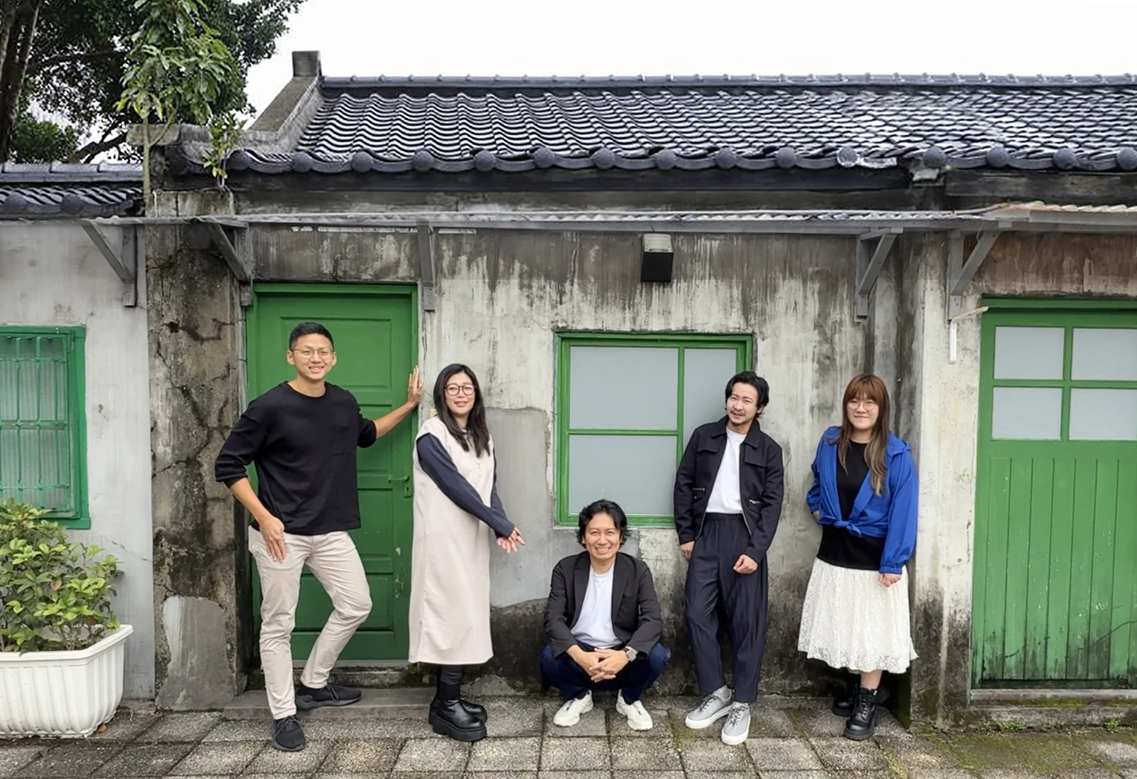 在有瓦片屋頂與綠色木門的老屋前,五位成員並排站著